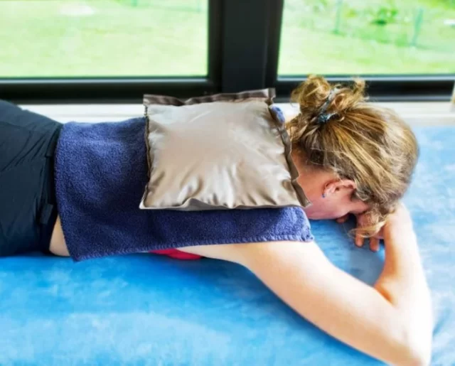 Mujer acostada boca abajo aplicando terapia de calor o frío como tratamiento para la neuritis intercostal